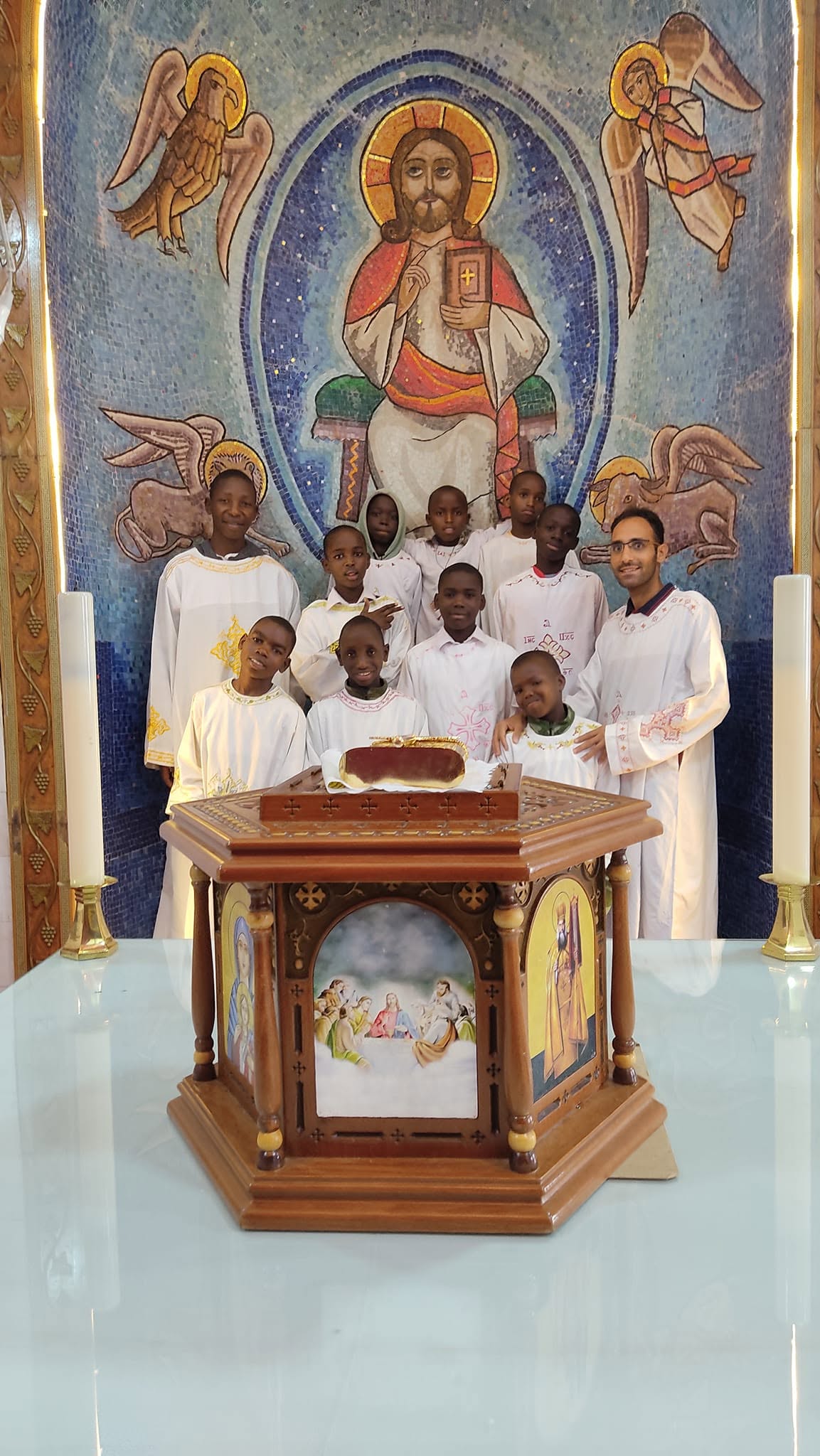 Boys in white robes serving at the altar beneath a mosaic of Christ