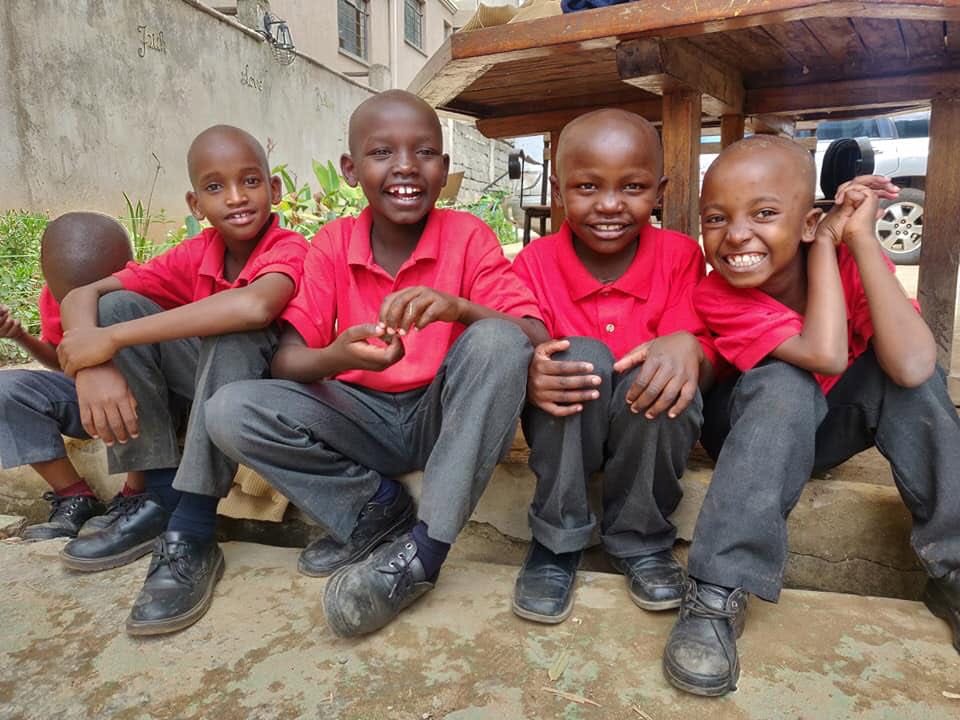 Four boys in red shirts sitting together on a step, laughing