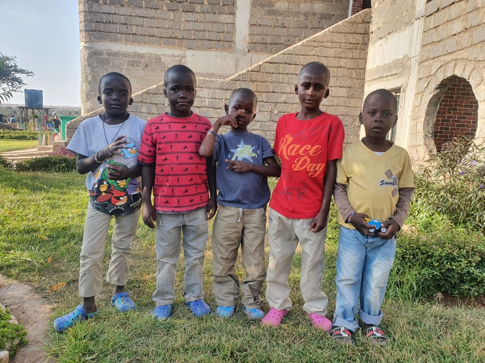 Five young boys standing together on the grass outside the Raha Kids home